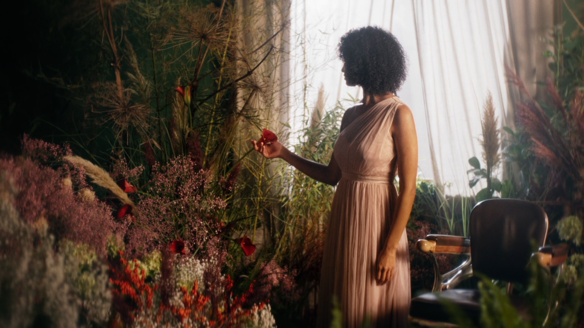 This is a screenshot of the Film "Ritual". It shows the protagonist in the middle of beautiful flowers and in the background we see a very old chair from a saloon.