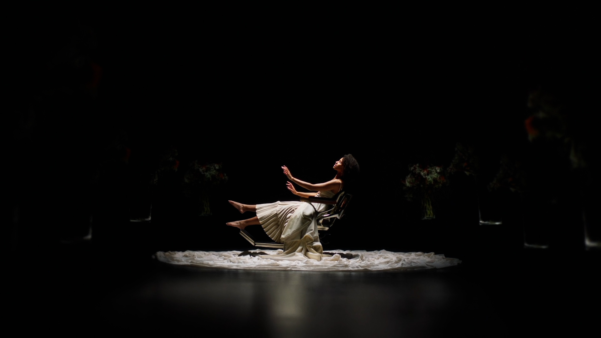 This screen grab shows the very last shot of the commercial. The protagonist is in the chair we saw in the first shot of the saloon. Around her darkness in which flowers lift from the ground.